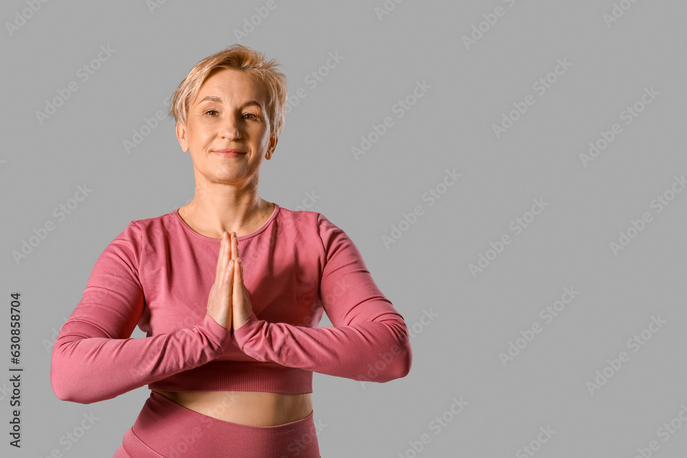 Sporty mature woman practicing yoga on grey background