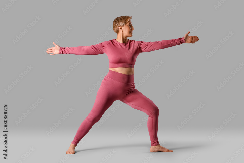 Sporty mature woman practicing yoga on grey background