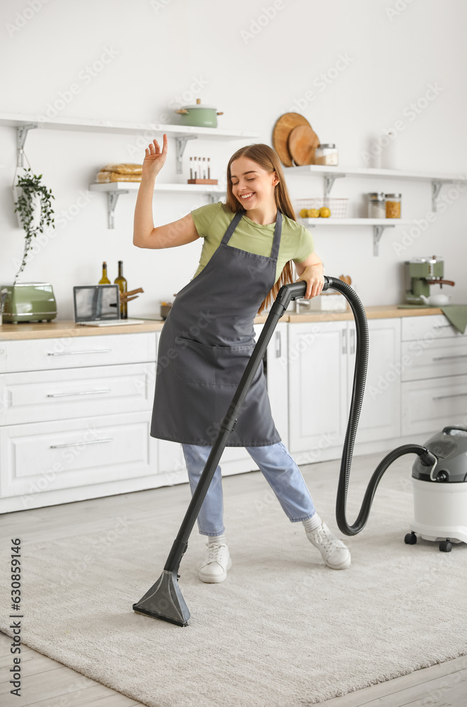 Young woman with vacuum cleaner dancing in kitchen