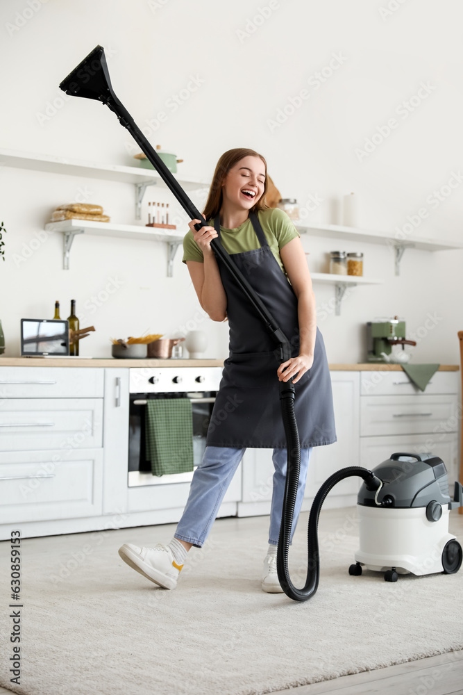 Young woman with vacuum cleaner dancing in kitchen