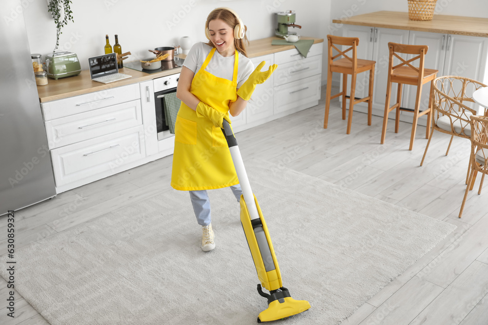 Young woman with headphones hoovering carpet in kitchen