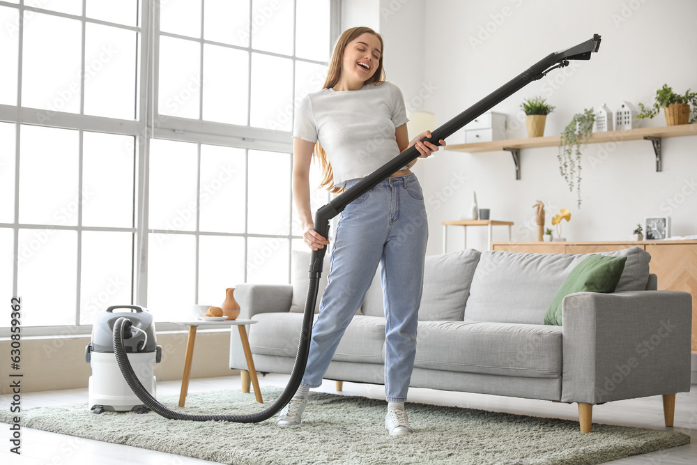 Young woman with vacuum cleaner singing at home