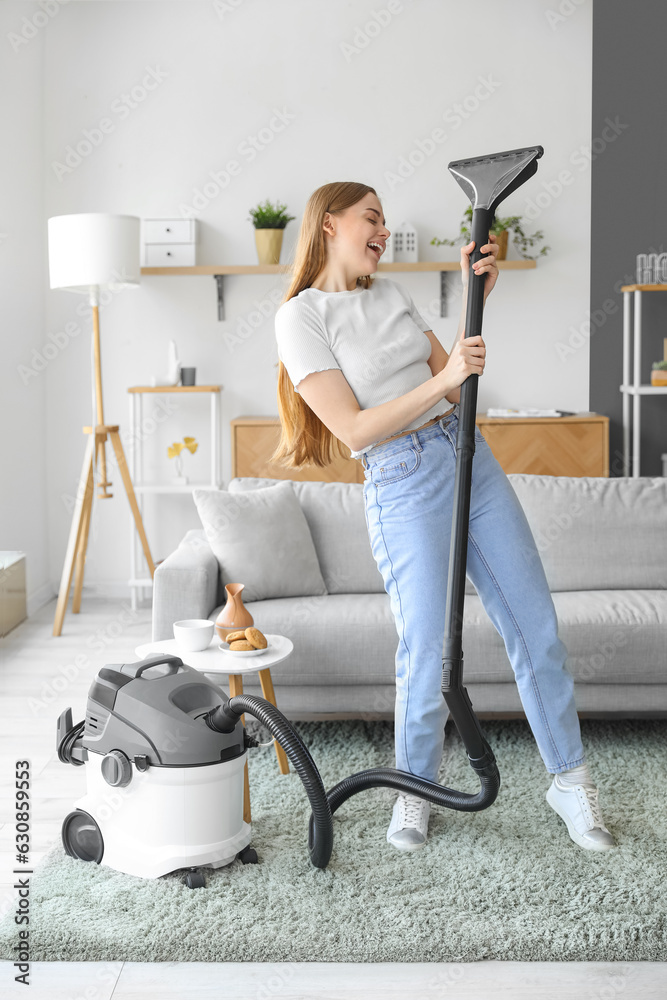 Young woman with vacuum cleaner singing at home