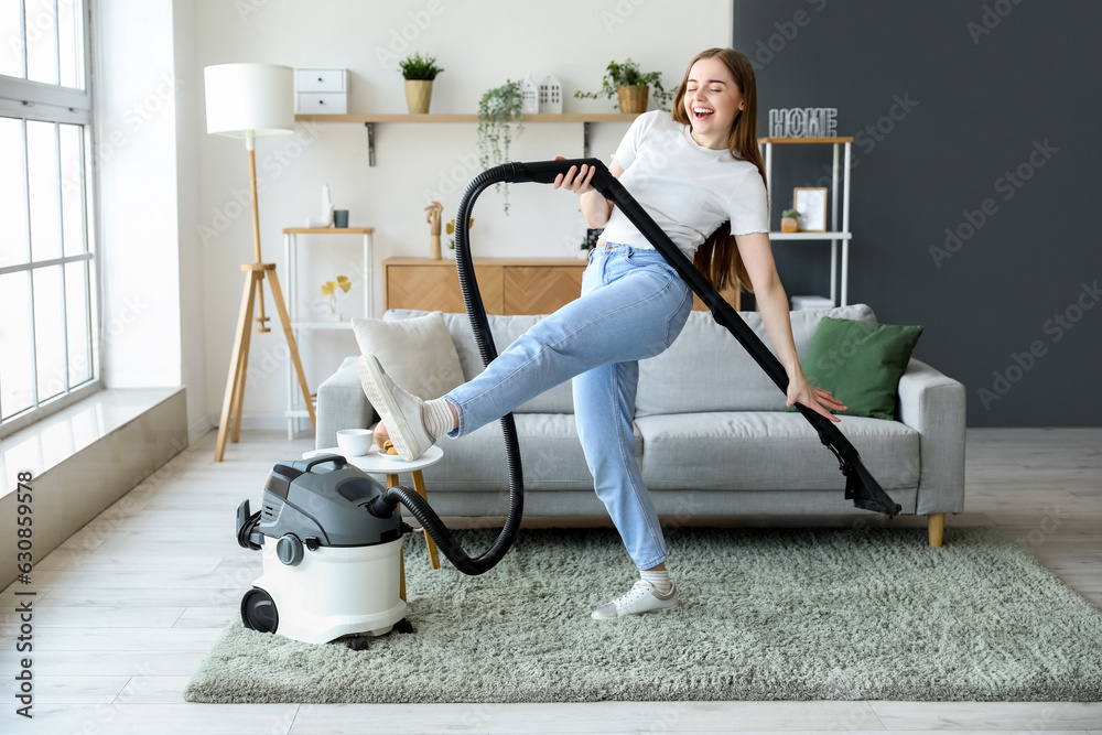 Young woman with vacuum cleaner dancing at home