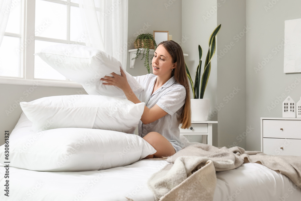 Morning of pretty young woman stacking soft pillows in bedroom