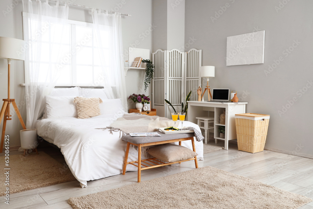 Interior of light bedroom with breakfast and workplace