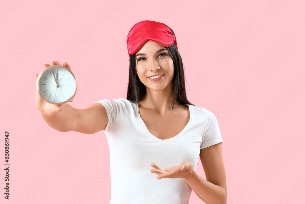 Young woman with sleeping mask and alarm clock on pink background