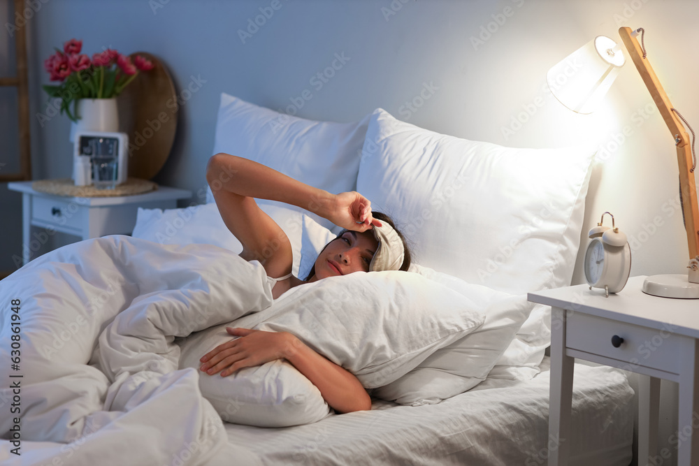 Young woman with sleeping mask lying in bed at night