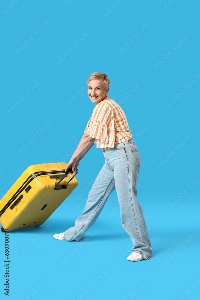 Mature woman with suitcase on blue background