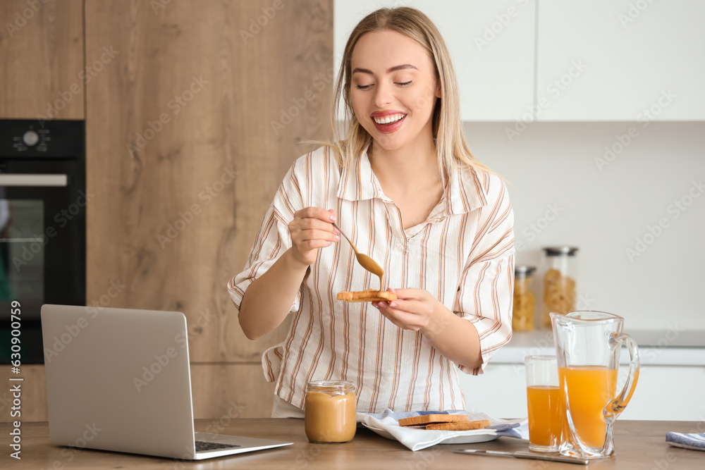 Young woman spreading tasty nut butter onto toast in kitchen