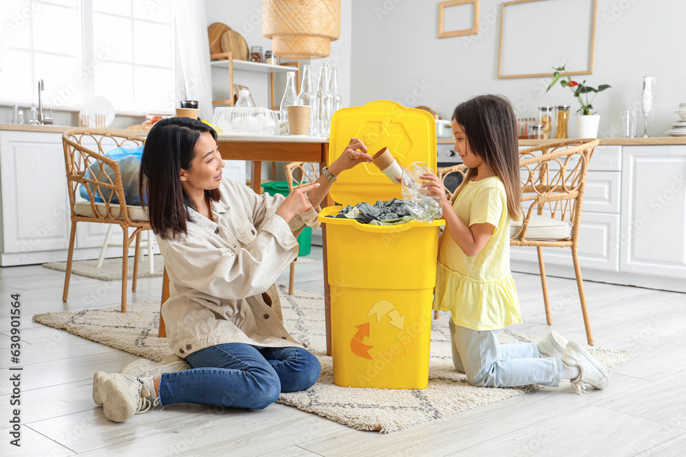 Asian mother with her little daughter sorting garbage with recycle bin in kitchen