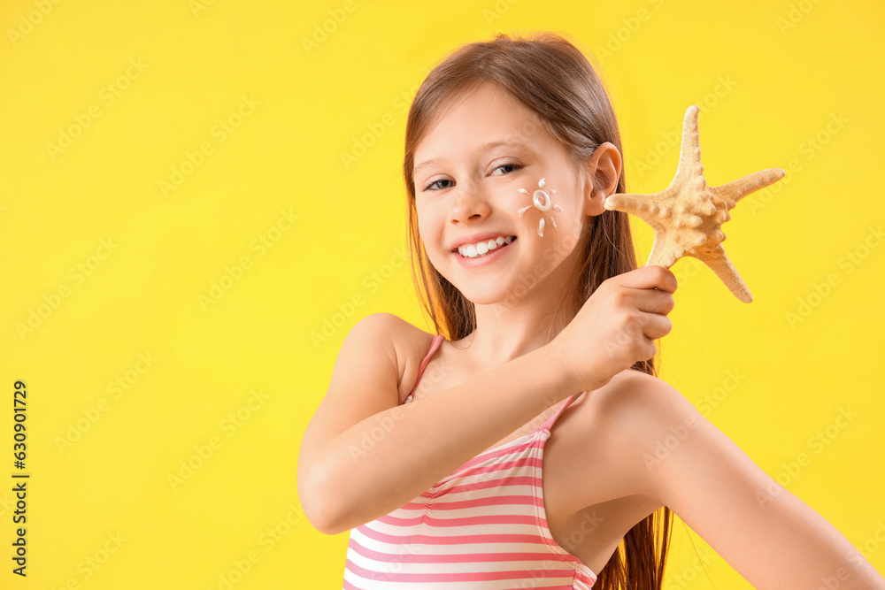 Little girl with starfish and sunscreen cream on her face on yellow background