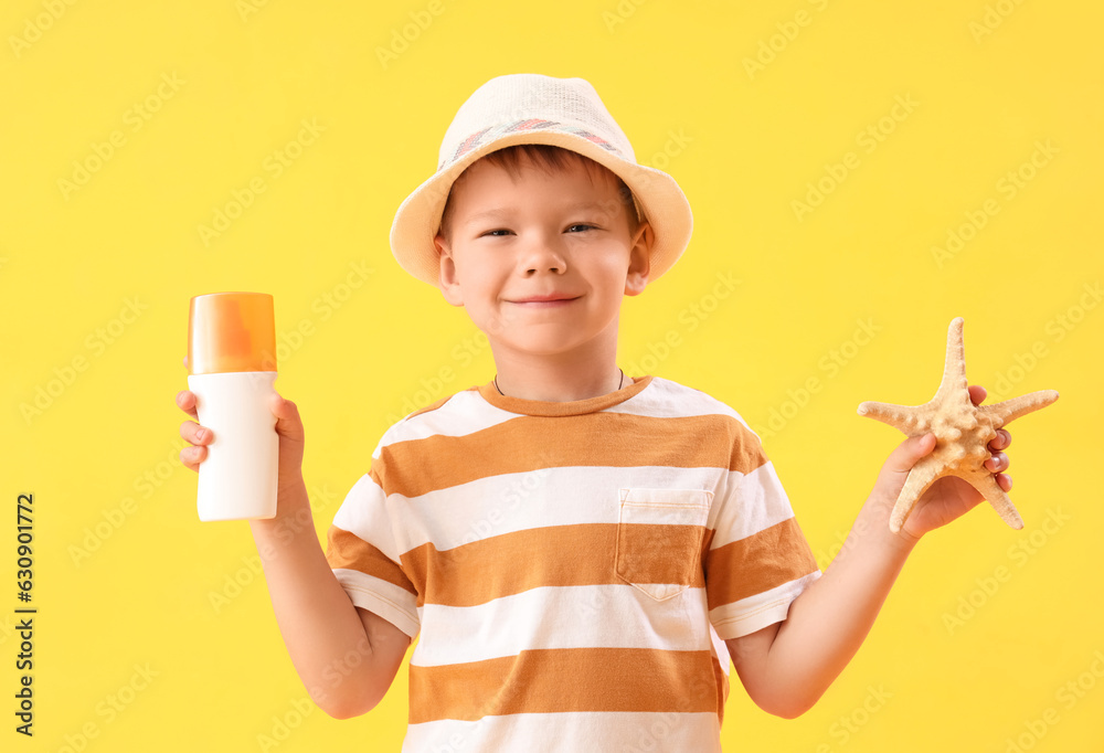 Little boy with bottle of sunscreen cream and starfish on yellow background