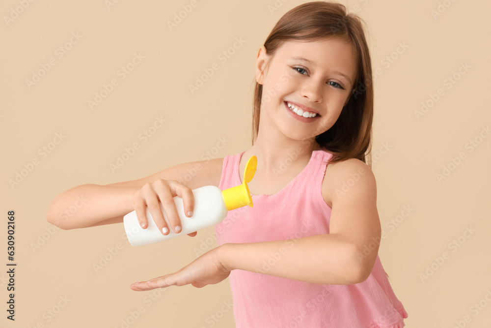 Little girl applying sunscreen cream on beige background