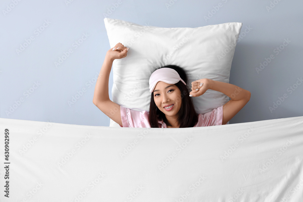 Beautiful Asian woman with pillow and blanket on grey background