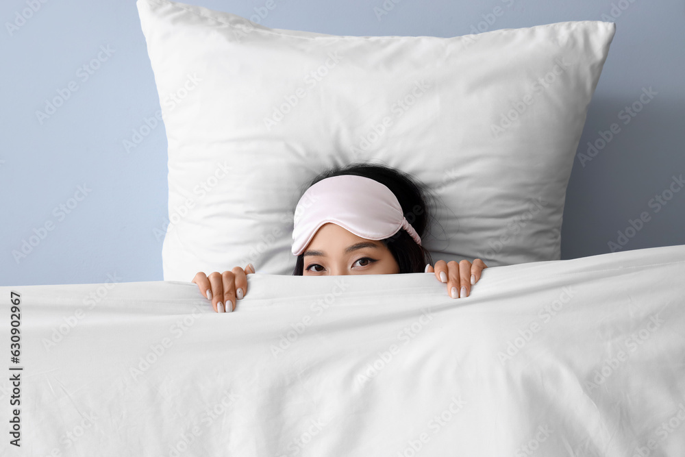 Beautiful Asian woman with pillow and blanket on grey background