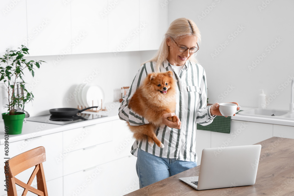 Mature woman with Pomeranian dog and cup of coffee in kitchen