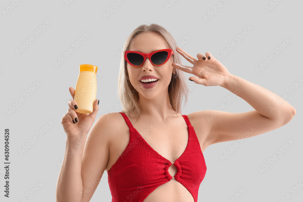 Young woman with sunscreen cream showing victory gesture on light background