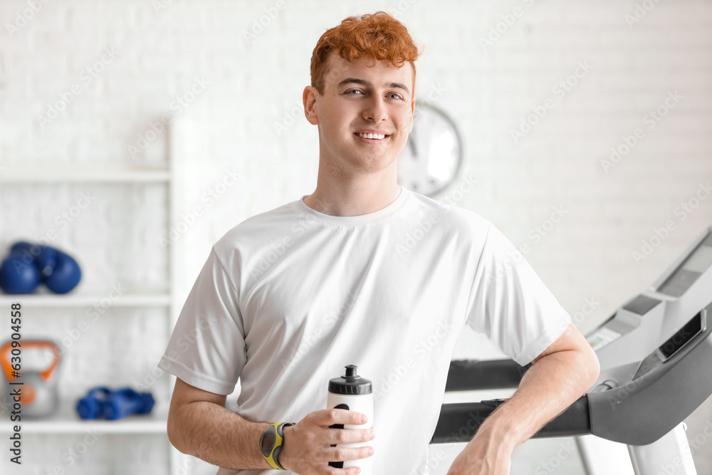 Young redhead man with sports water bottle in gym