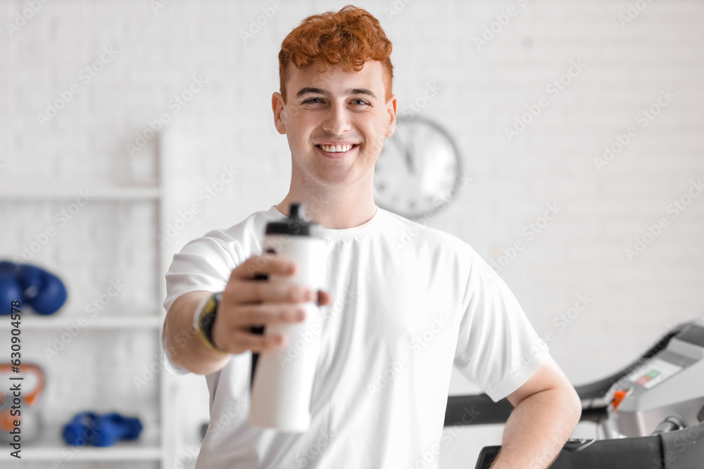 Young redhead man with sports water bottle in gym