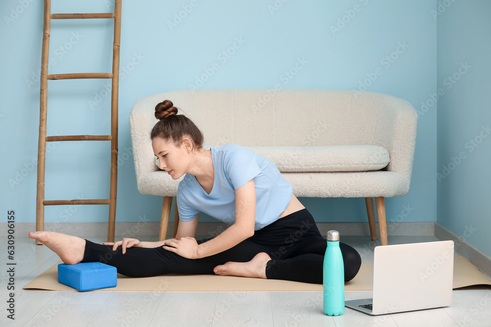 Sporty young woman stretching with yoga block at home