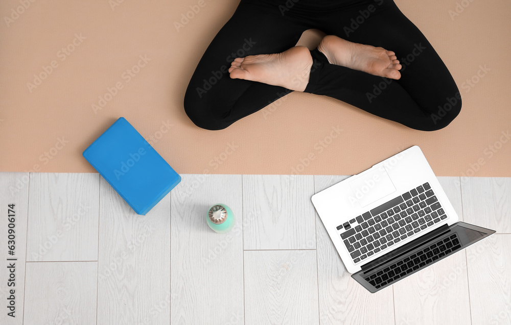 Woman with yoga block, bottle and laptop sitting on mat, top view