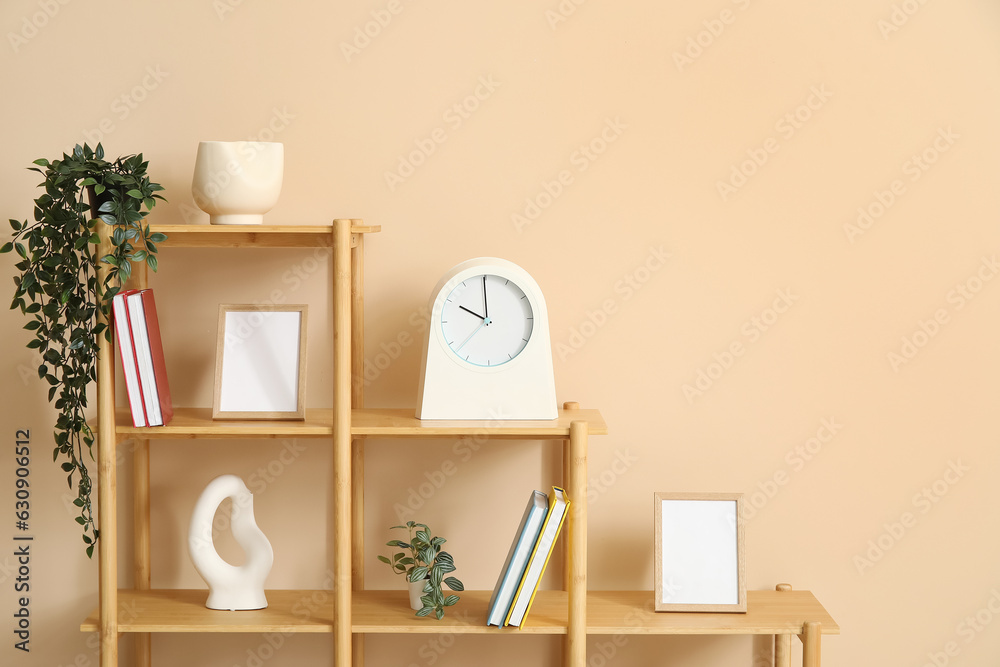 Wooden shelf with books, clock and decor near beige wall