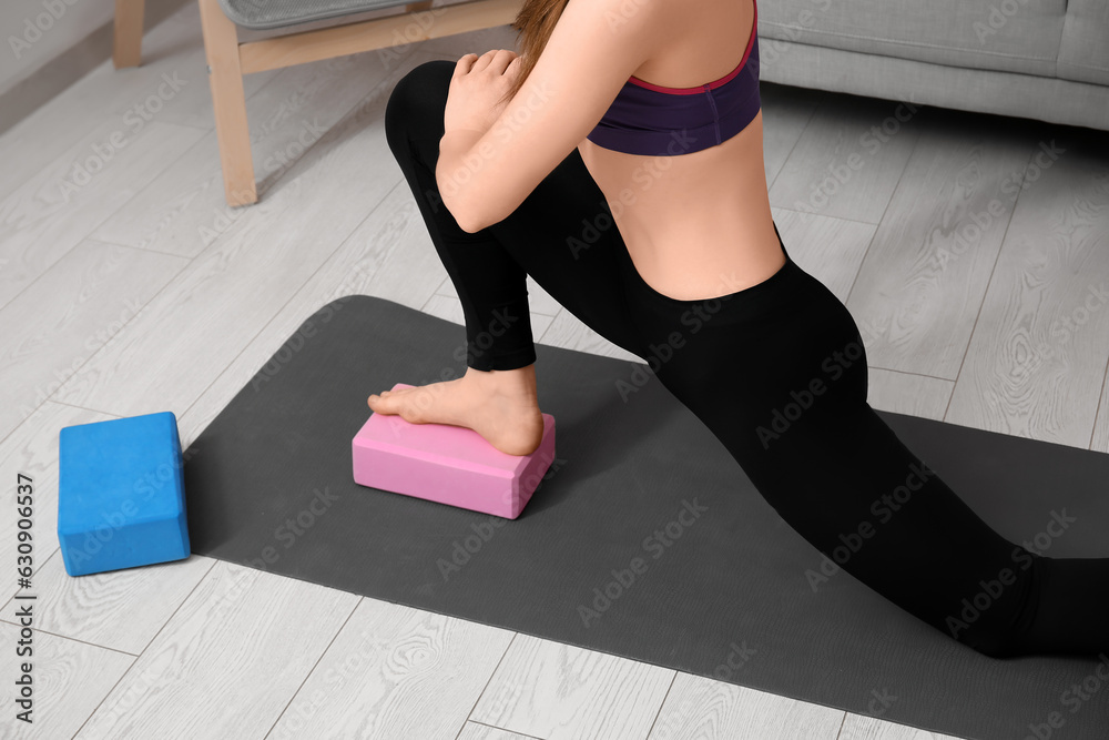 Sporty young woman practicing yoga with block at home