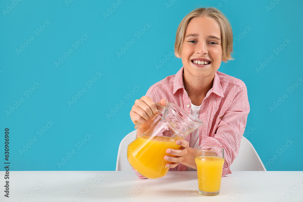 Little boy pouring orange juice into glass at table on blue background