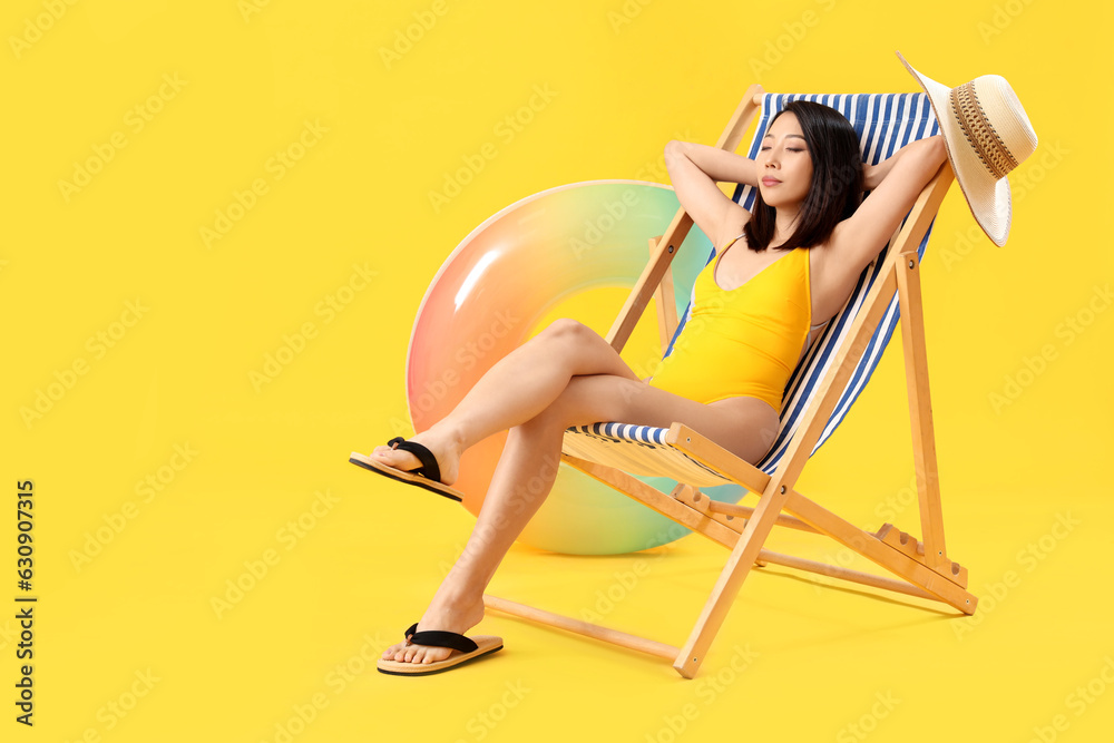 Beautiful Asian woman relaxing in deck chair on yellow background