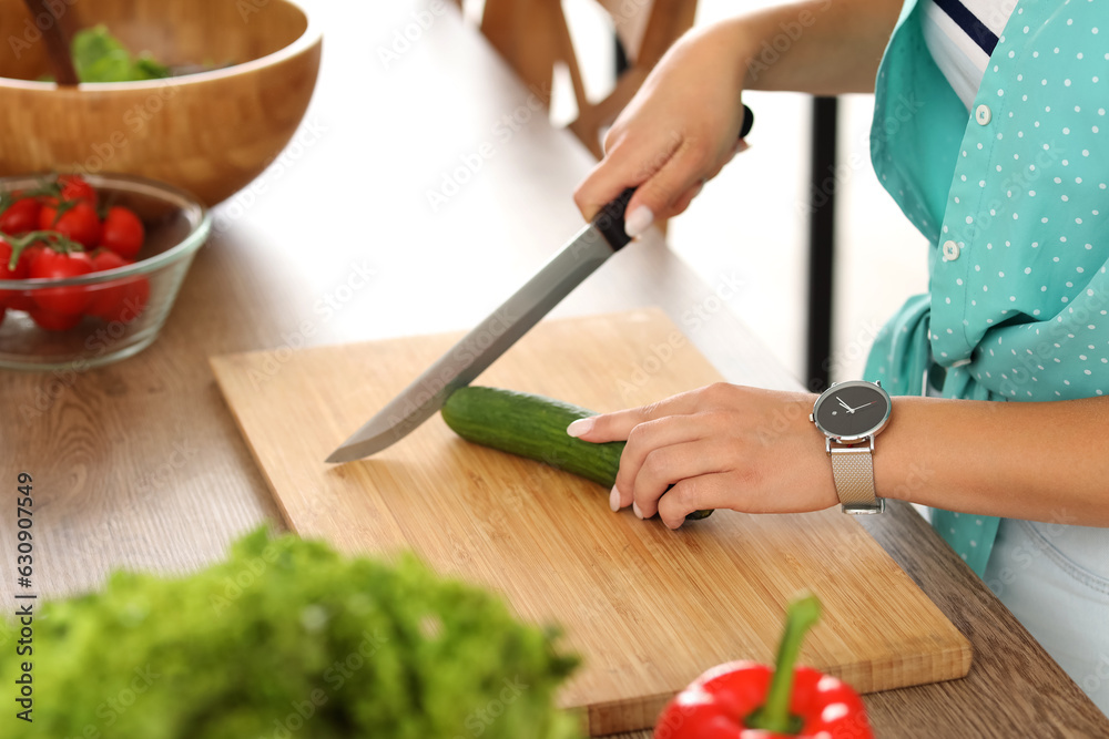 Young woman cutting cucumber for salad in kitchen, closeup