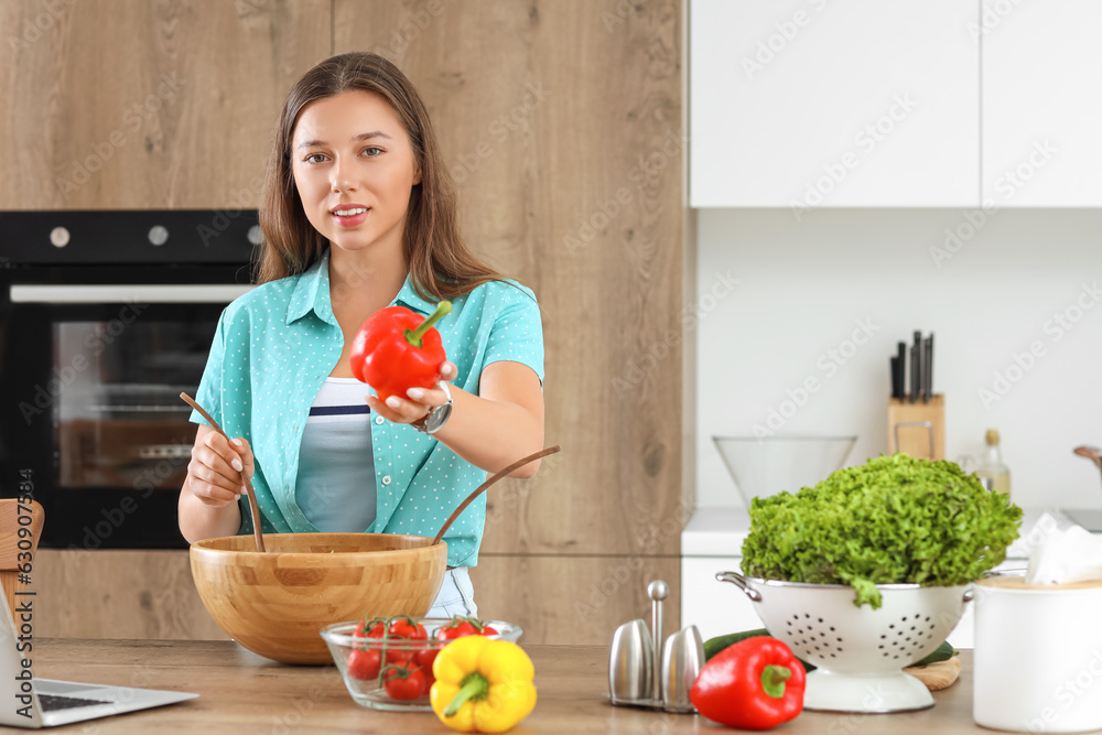 Young woman preparing vegetable salad in kitchen