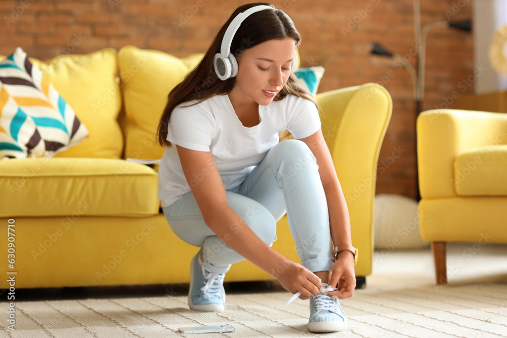 Young woman in headphones tying shoe laces at home