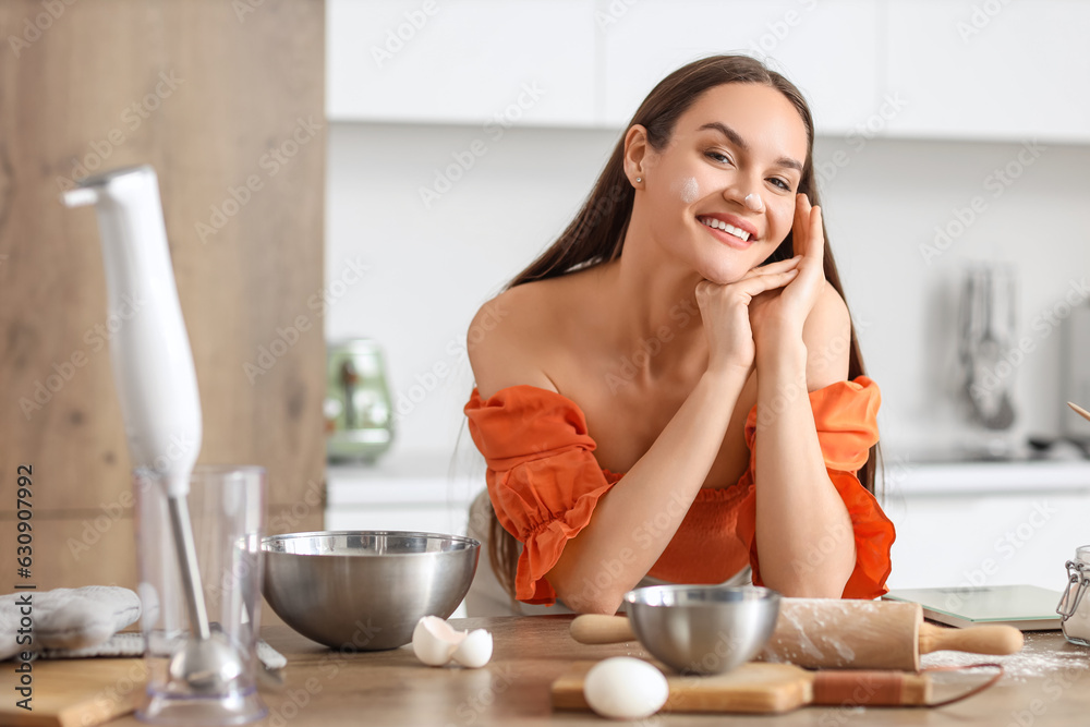 Young woman with flour on her face preparing dough in kitchen