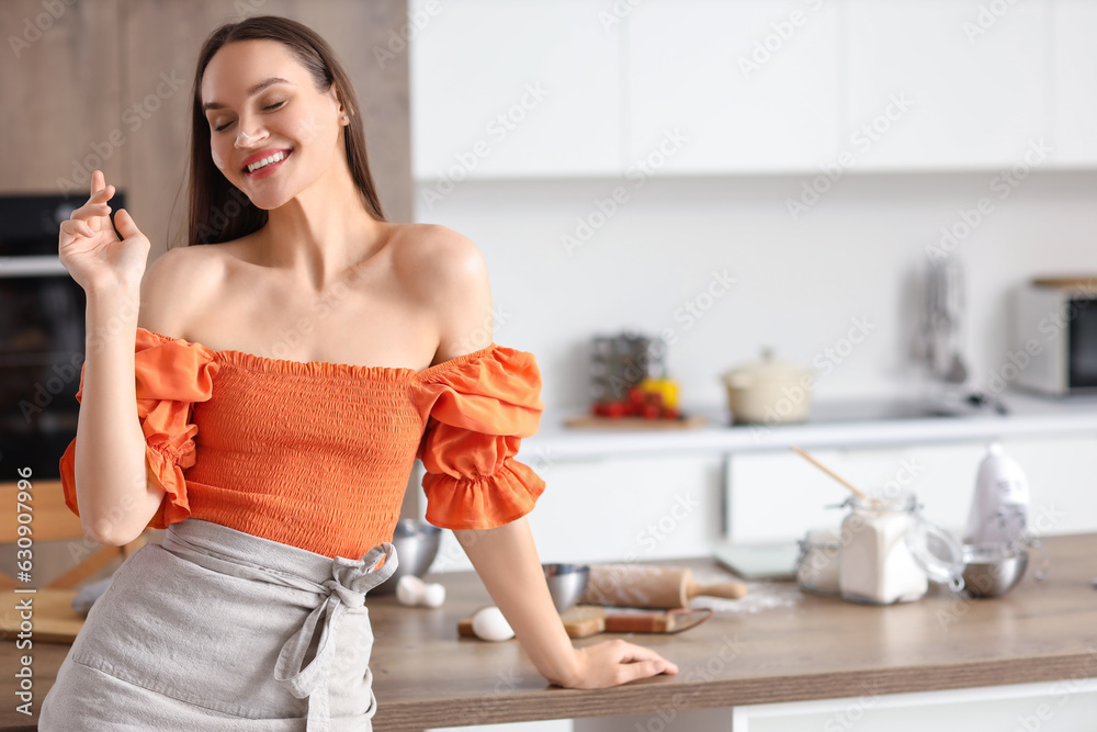 Young woman with flour on her face preparing dough in kitchen