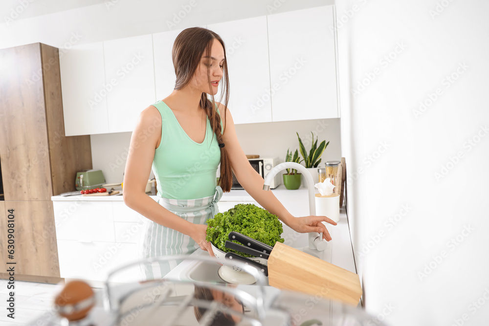 Young woman washing fresh lettuce in kitchen