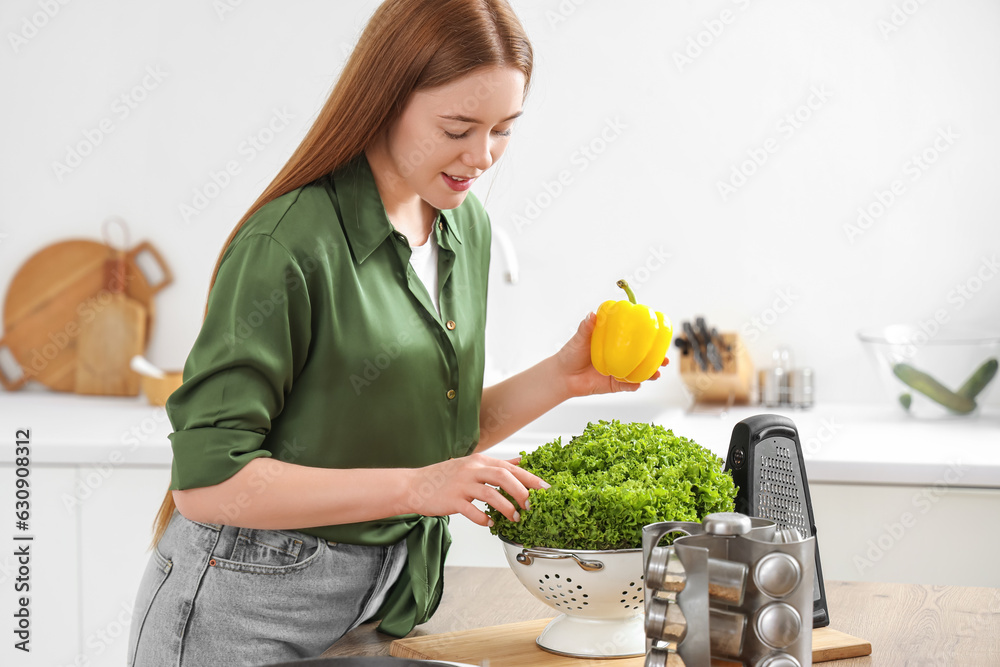 Young woman with fresh lettuce and bell pepper in kitchen