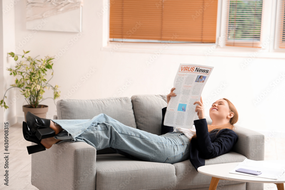 Young businesswoman reading newspaper at home after long working day