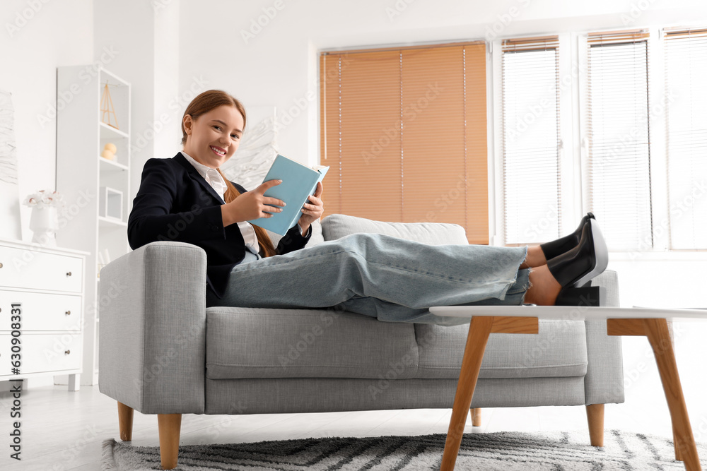 Young businesswoman reading book at home after long working day