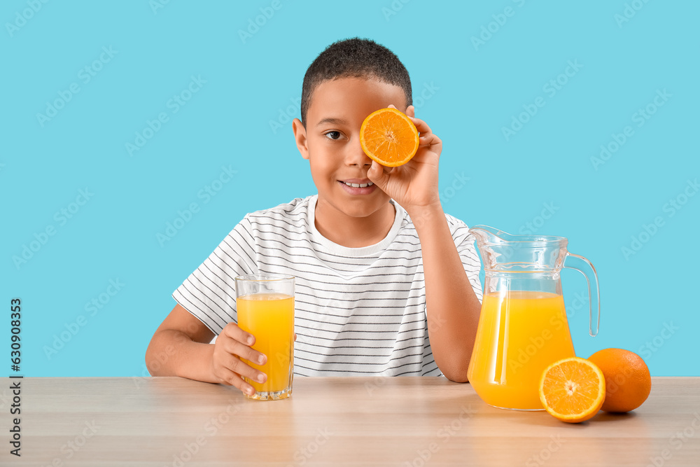 Little African-American boy with glass of orange juice at table on blue background