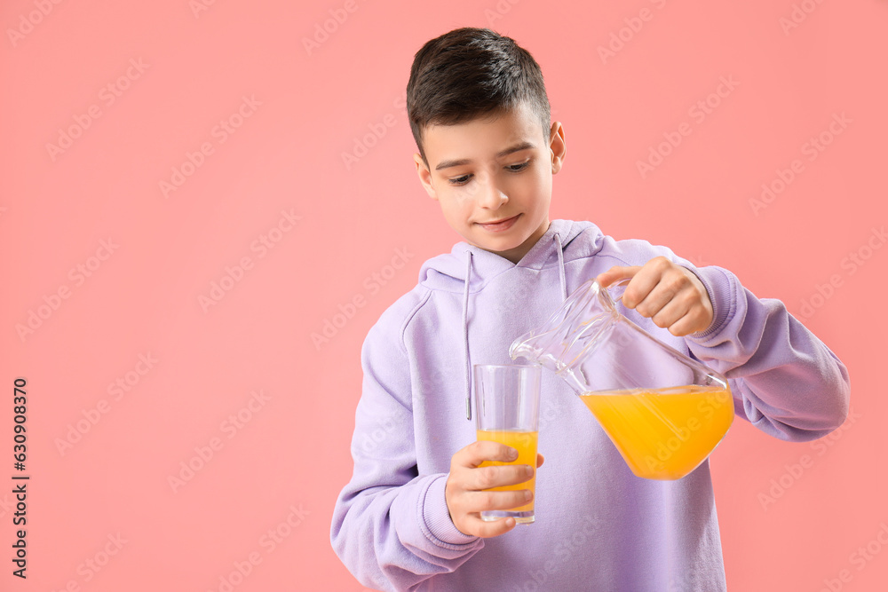 Little boy pouring orange juice into glass on pink background