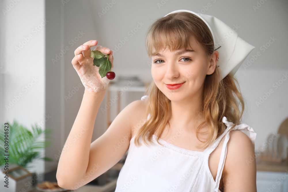 Happy beautiful young woman with branch of cherry in kitchen