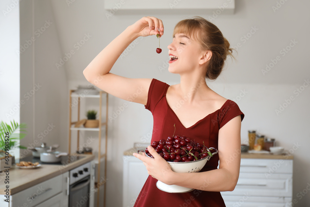 Beautiful happy young woman eating ripe cherries in kitchen