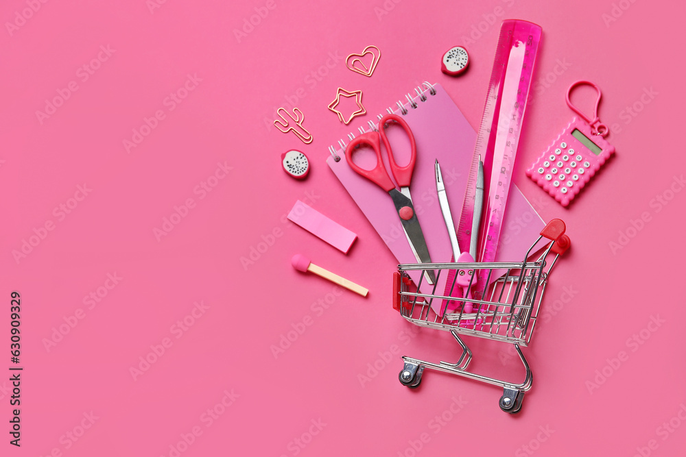 Composition with shopping cart and different stationery on pink background