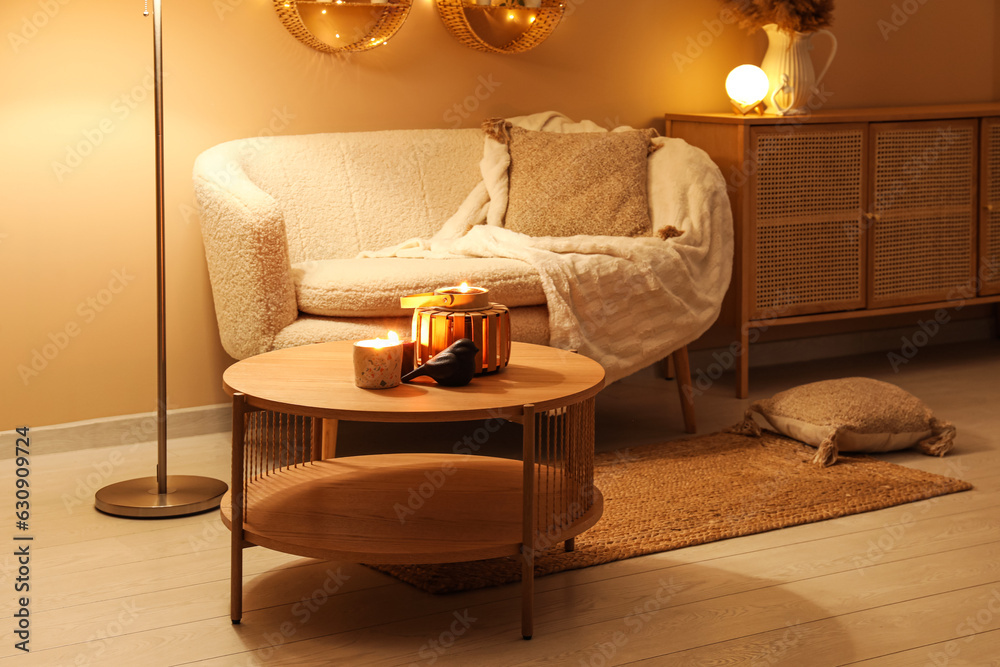 Modern interior of living room with stylish sofa and burning candles on table