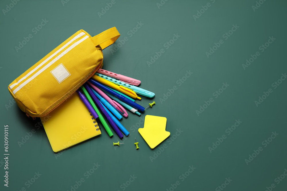 Pencil case with different school stationery on green background