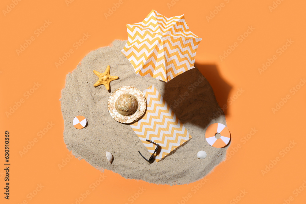 Creative summer composition with mini umbrella, beach accessories and sand on orange background