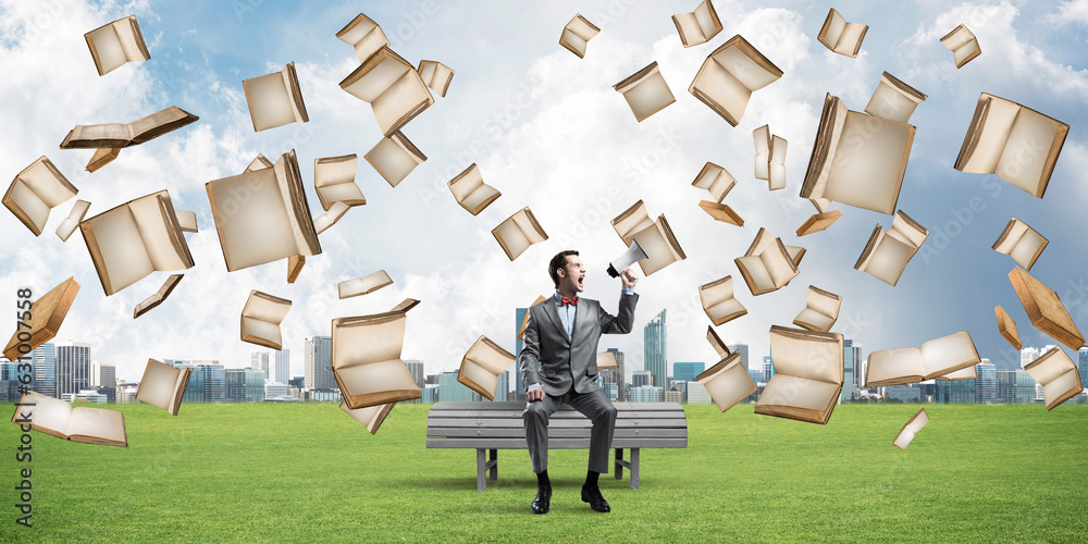 Businessman in summer park announcing something in loudspeaker and books falling from above