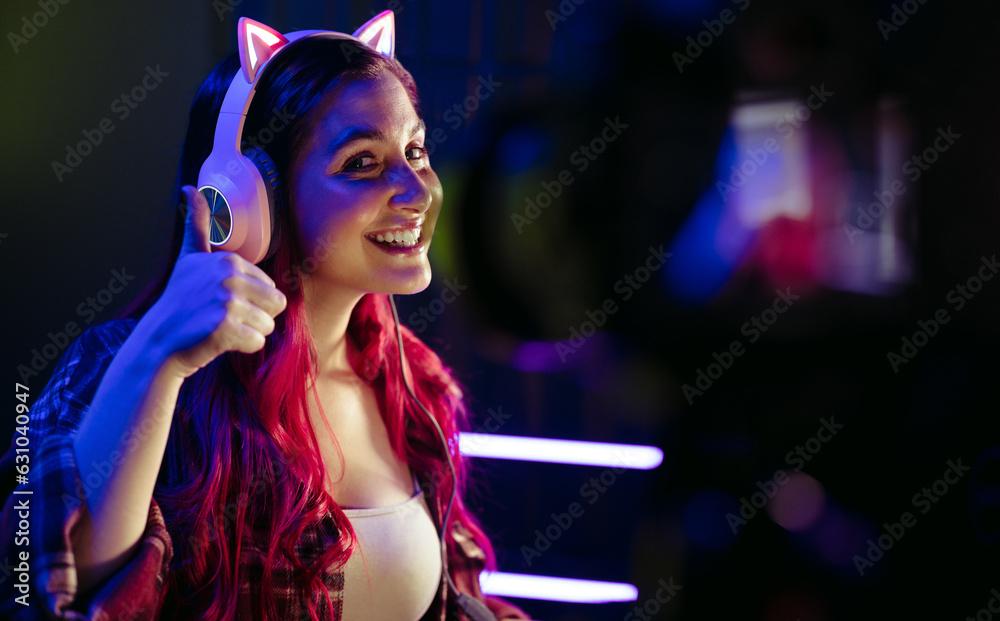 Happy female gamer doing a thumbs up for the camera as she lice records a gaming session