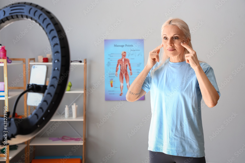 Mature physiotherapist doing face building exercise while recording video in rehabilitation center